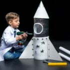 Little boy in white coat drilling toy rocket with toy drill
