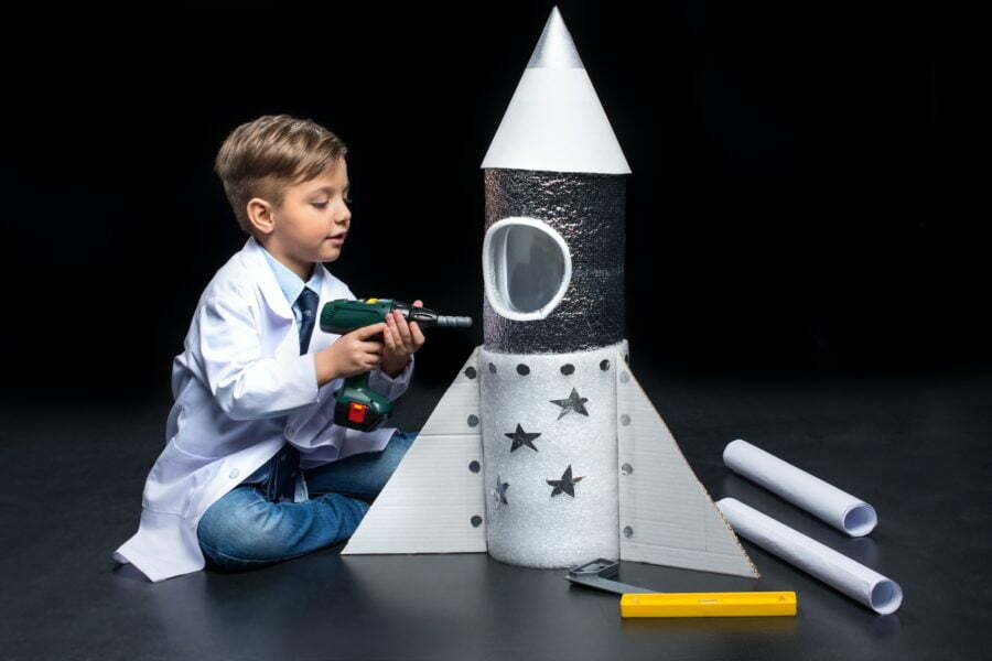 Little boy in white coat drilling toy rocket with toy drill